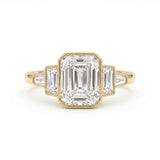 Emerald-cut lab-grown diamond five-stone engagement ring with emerald side stones, tapered baguettes and milgrain yellow-gold settings.