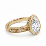 Vintage pear-cut lab-grown diamond bezel engagement ring with milgrain, scroll filigree and round diamond accents on a yellow-gold band.