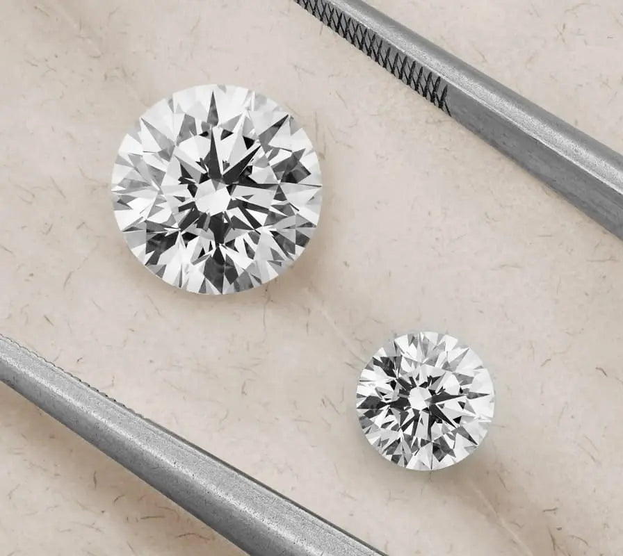 Two loose round brilliant cut diamonds held with tweezers
