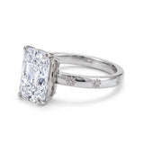 Radiant-cut solitaire engagement ring with four claw prongs and daisy flower engravings on a polished white-metal band