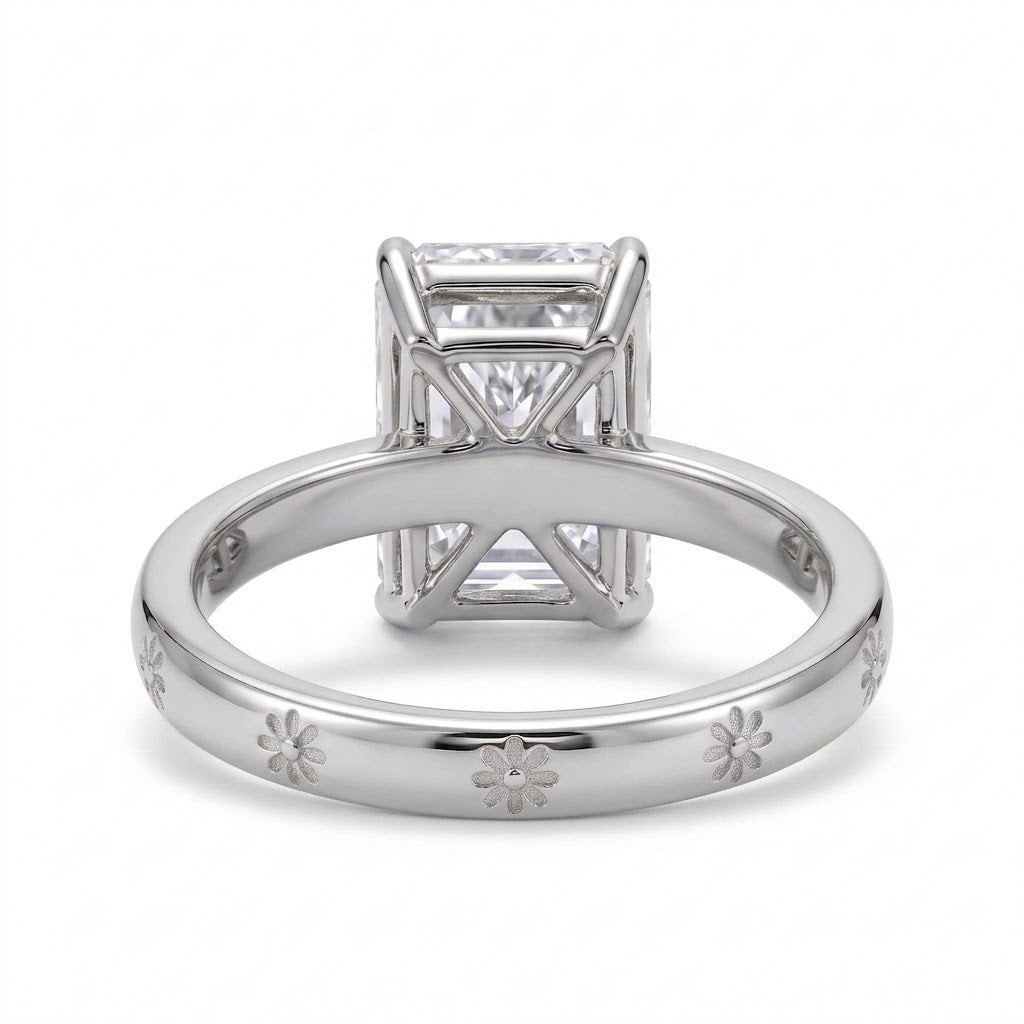Radiant-cut solitaire engagement ring with four claw prongs and daisy flower engravings on a polished white-metal band