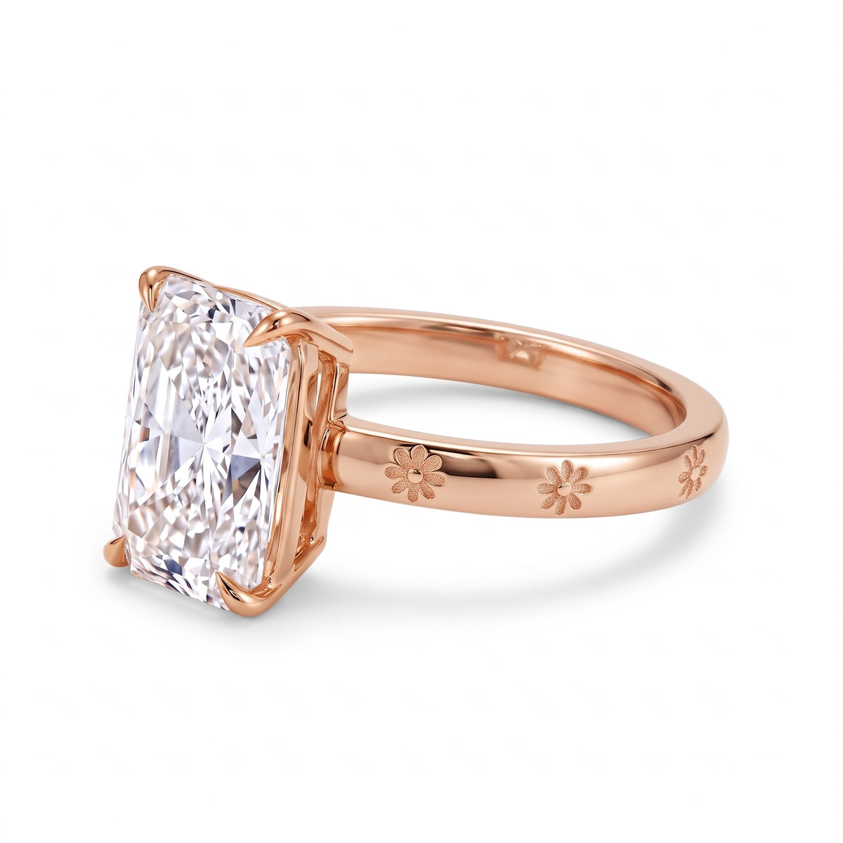 Radiant-cut solitaire engagement ring with four claw prongs and daisy flower engravings on a polished white-metal band