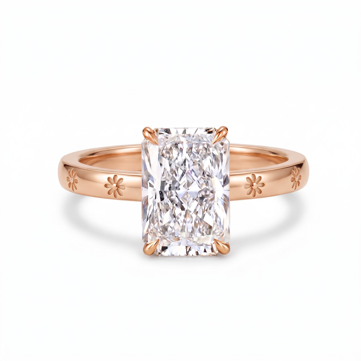 Radiant-cut solitaire engagement ring with four claw prongs and daisy flower engravings on a polished white-metal band
