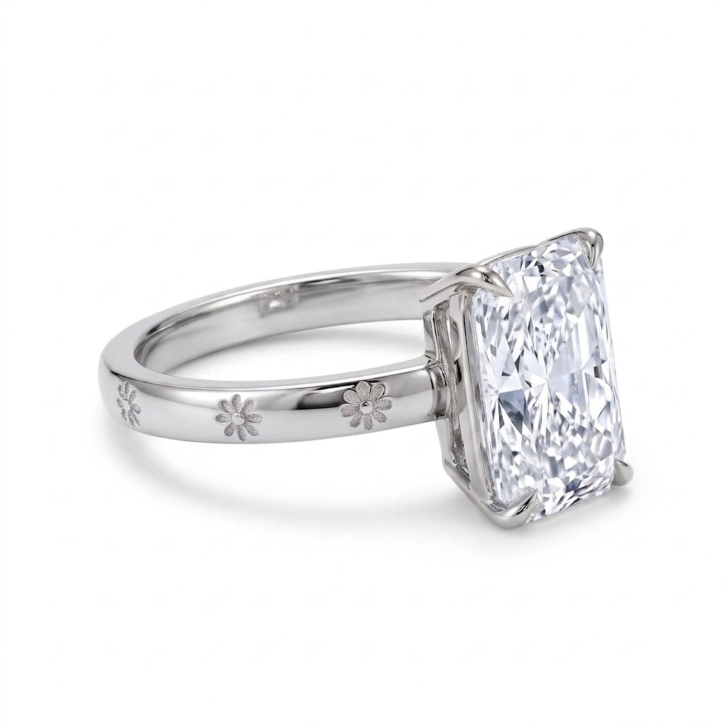 Radiant-cut solitaire engagement ring with four claw prongs and daisy flower engravings on a polished white-metal band