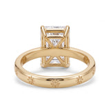 Radiant-cut solitaire engagement ring with four claw prongs and daisy flower engravings on a polished white-metal band