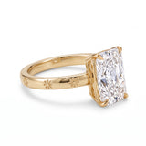 Radiant-cut solitaire engagement ring with four claw prongs and daisy flower engravings on a polished white-metal band