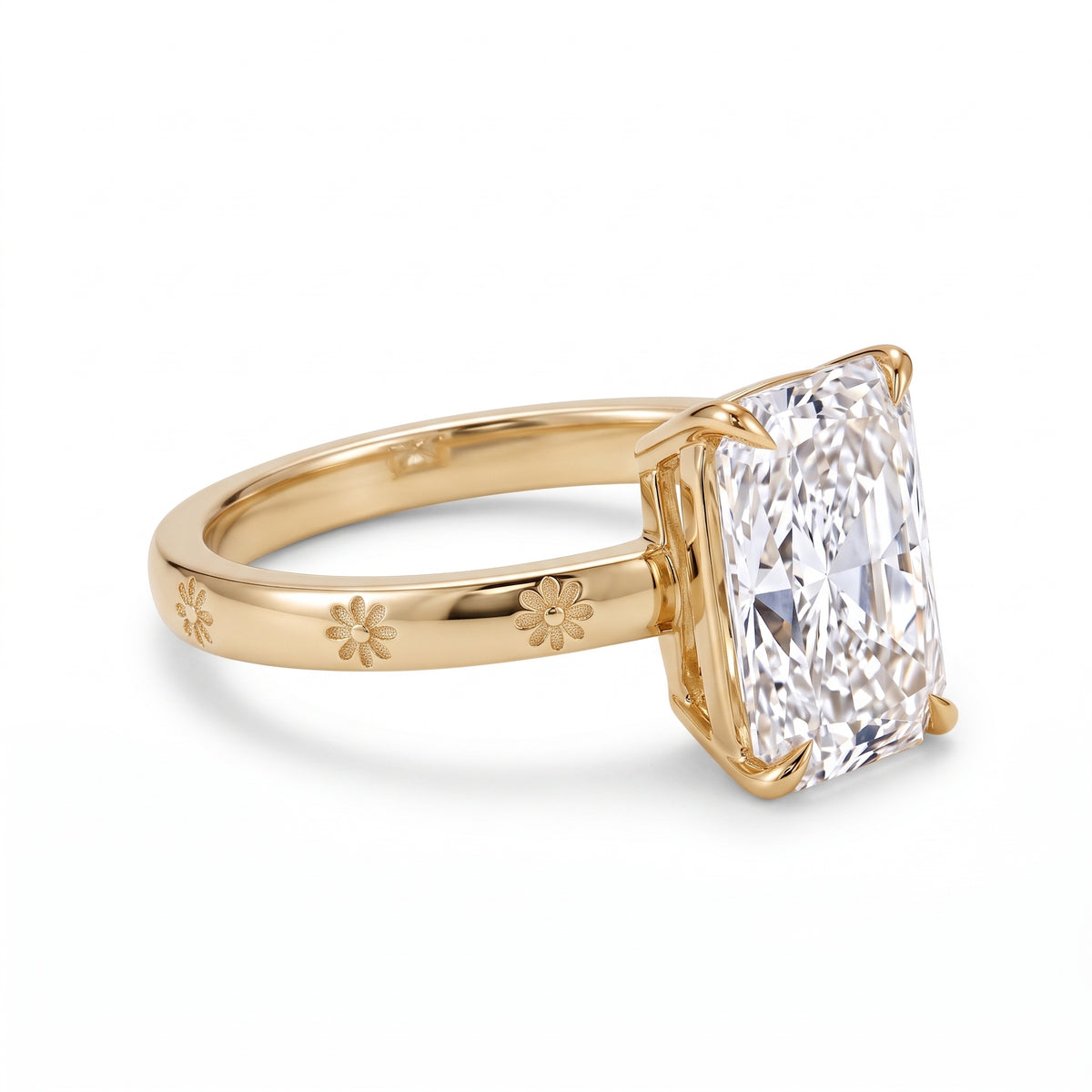 Radiant-cut solitaire engagement ring with four claw prongs and daisy flower engravings on a polished white-metal band