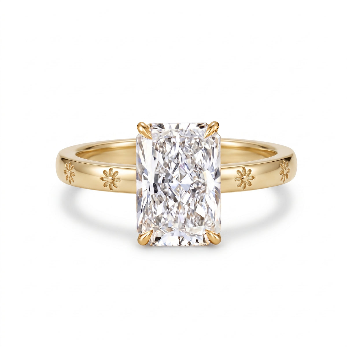 Radiant-cut solitaire engagement ring with four claw prongs and daisy flower engravings on a polished white-metal band