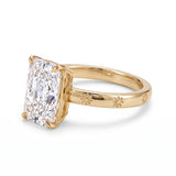 Radiant-cut solitaire engagement ring with four claw prongs and daisy flower engravings on a polished white-metal band