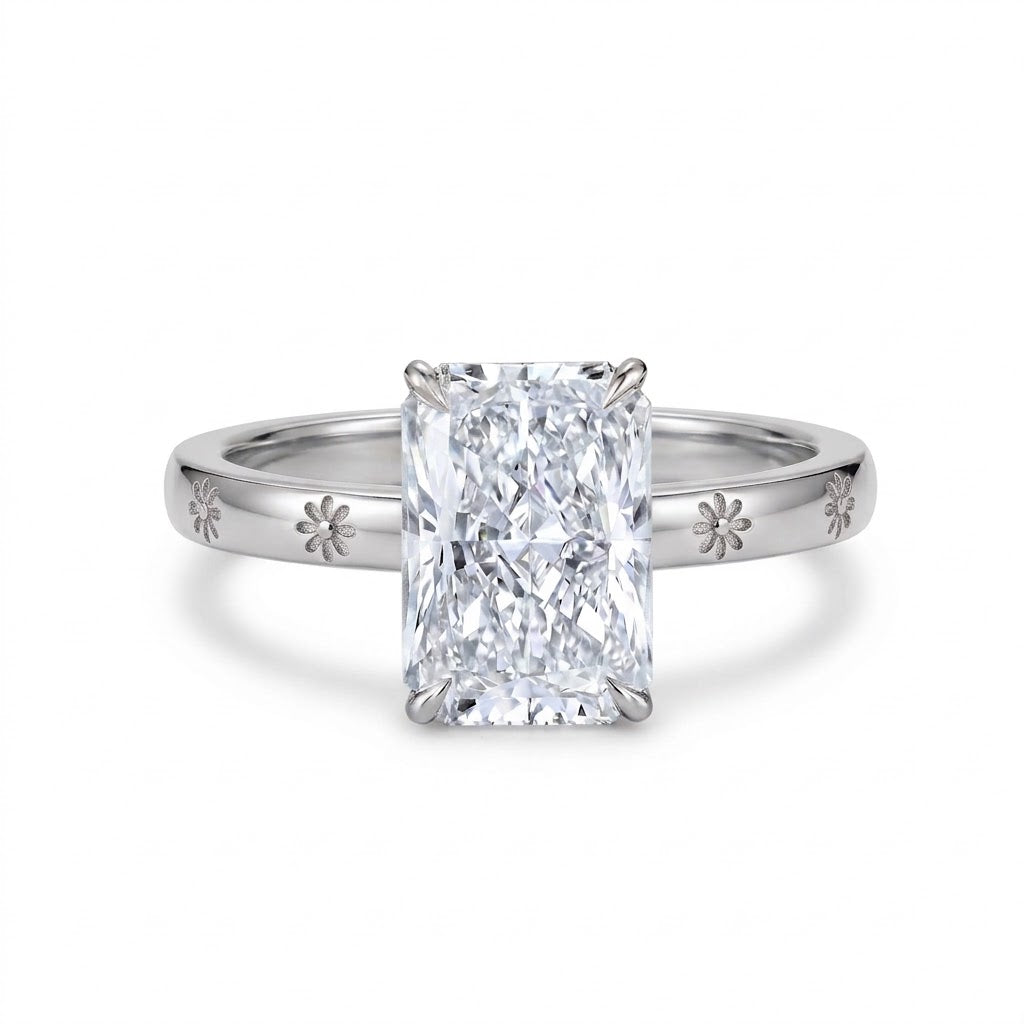 Radiant-cut solitaire engagement ring with four claw prongs and daisy flower engravings on a polished white-metal band