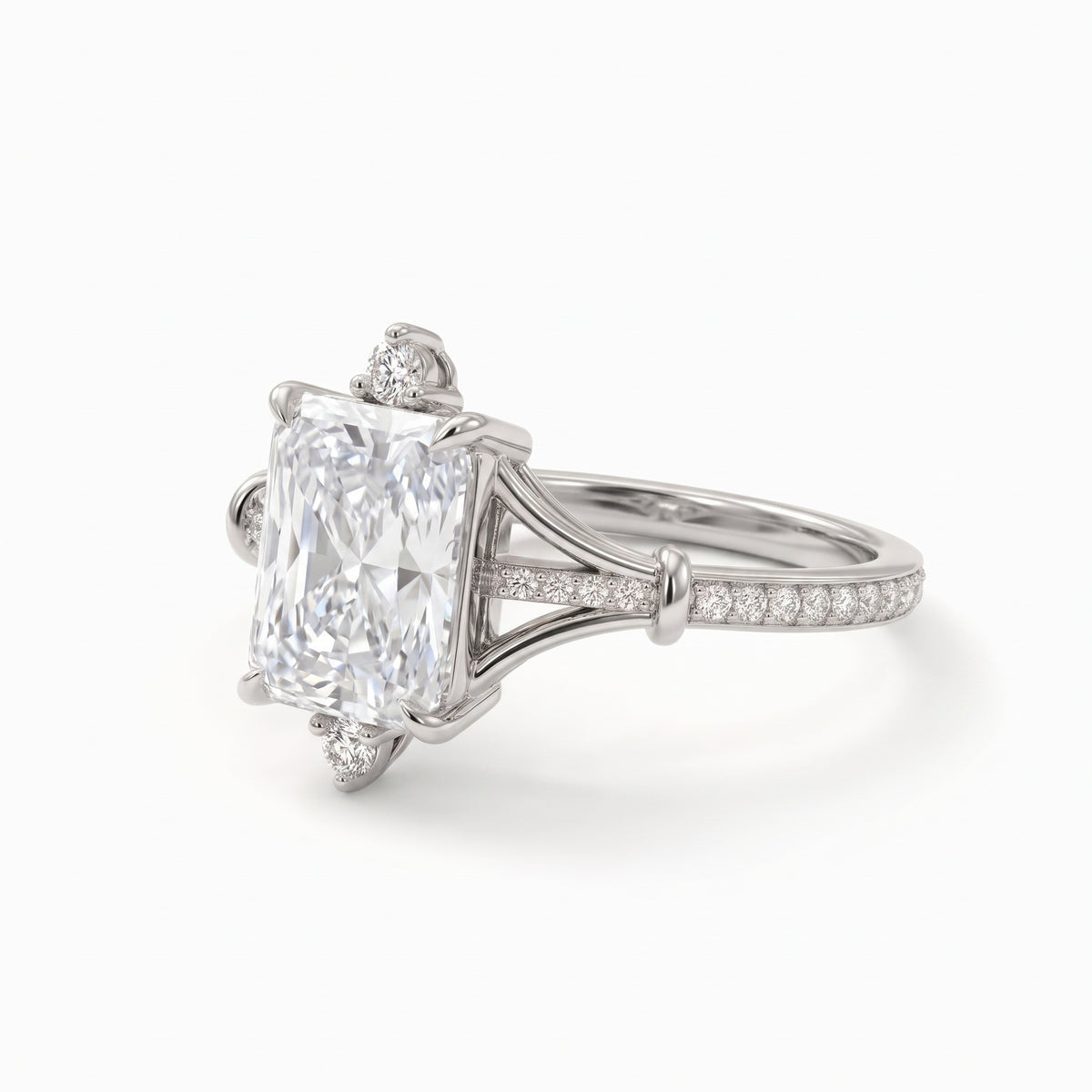 Radiant-cut engagement ring with pear-shaped accents above and below the center stone, pavé diamonds and polished white-metal split shoulders