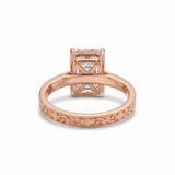Radiant-cut solitaire engagement ring with four claw prongs, floral scroll engravings and milgrain borders on a white-metal band