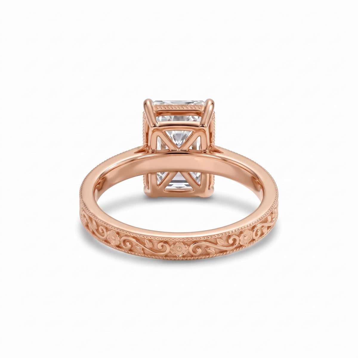 Radiant-cut solitaire engagement ring with four claw prongs, floral scroll engravings and milgrain borders on a white-metal band