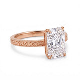 Radiant-cut solitaire engagement ring with four claw prongs, floral scroll engravings and milgrain borders on a white-metal band