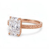 Radiant-cut solitaire engagement ring with four claw prongs, floral scroll engravings and milgrain borders on a white-metal band