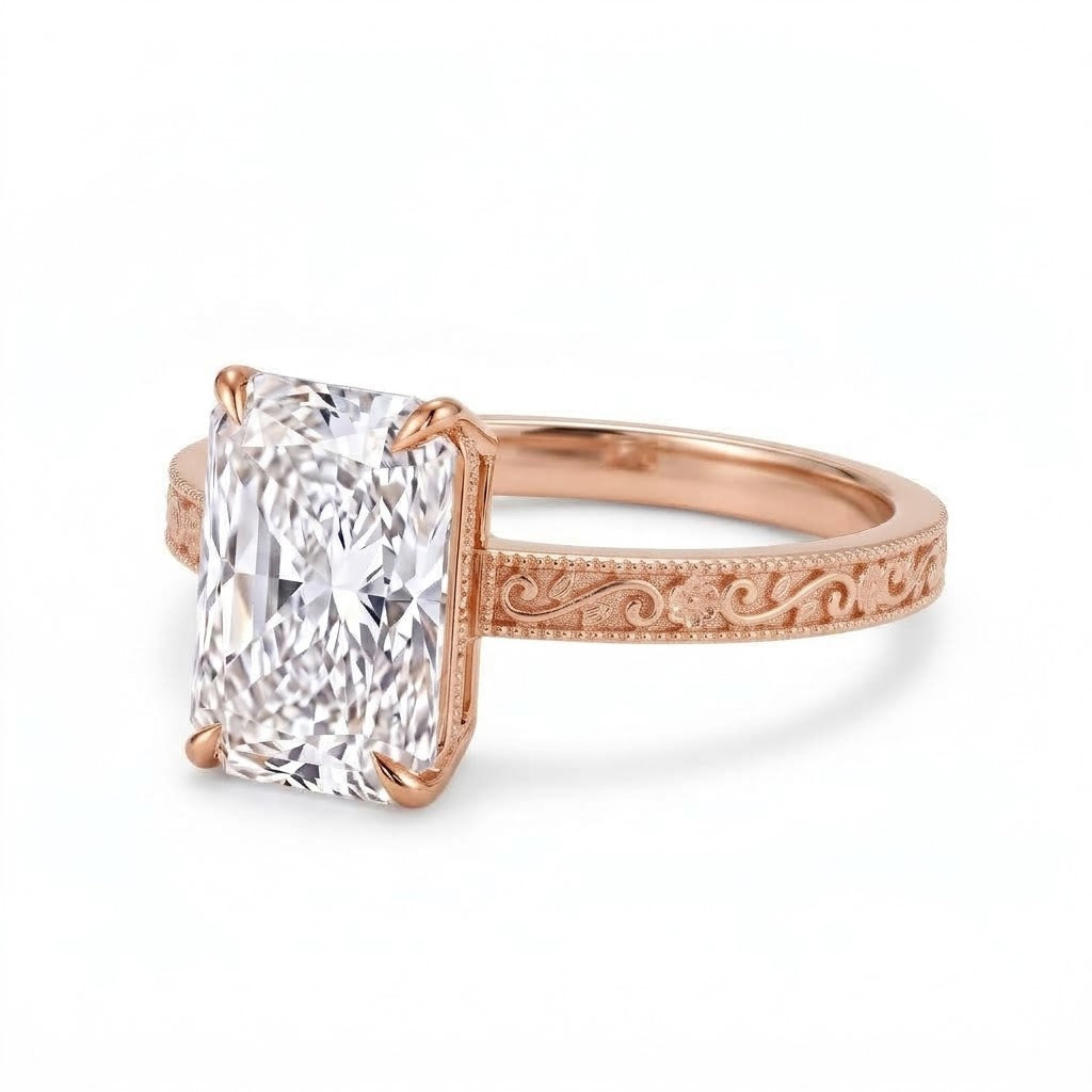 Radiant-cut solitaire engagement ring with four claw prongs, floral scroll engravings and milgrain borders on a white-metal band