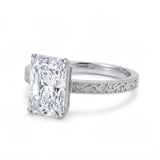Radiant-cut solitaire engagement ring with four claw prongs, floral scroll engravings and milgrain borders on a white-metal band