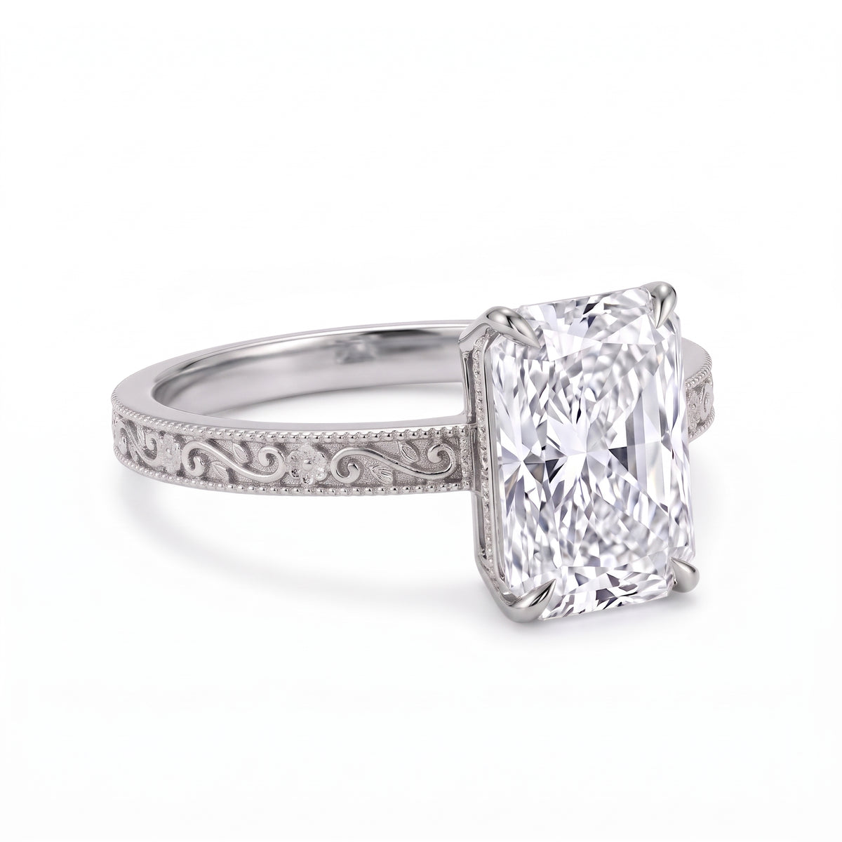 Radiant-cut solitaire engagement ring with four claw prongs, floral scroll engravings and milgrain borders on a white-metal band