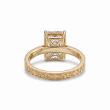 Radiant-cut solitaire engagement ring with four claw prongs, floral scroll engravings and milgrain borders on a white-metal band