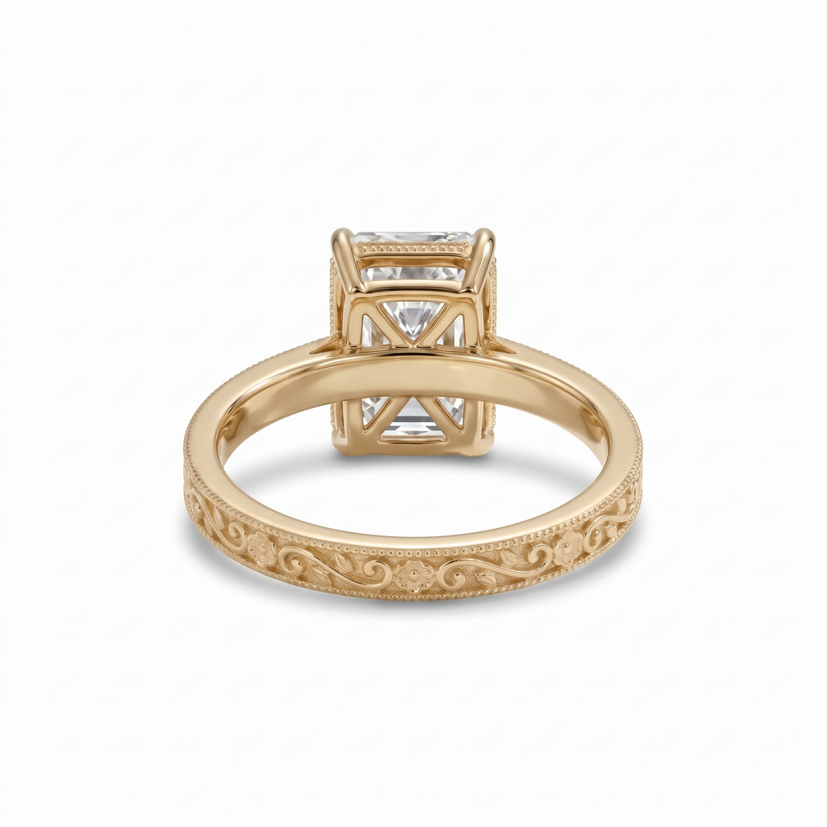 Radiant-cut solitaire engagement ring with four claw prongs, floral scroll engravings and milgrain borders on a white-metal band