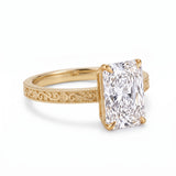 Radiant-cut solitaire engagement ring with four claw prongs, floral scroll engravings and milgrain borders on a white-metal band