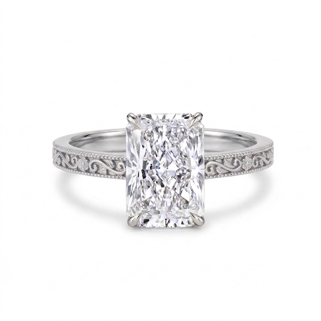 Radiant-cut solitaire engagement ring with four claw prongs, floral scroll engravings and milgrain borders on a white-metal band